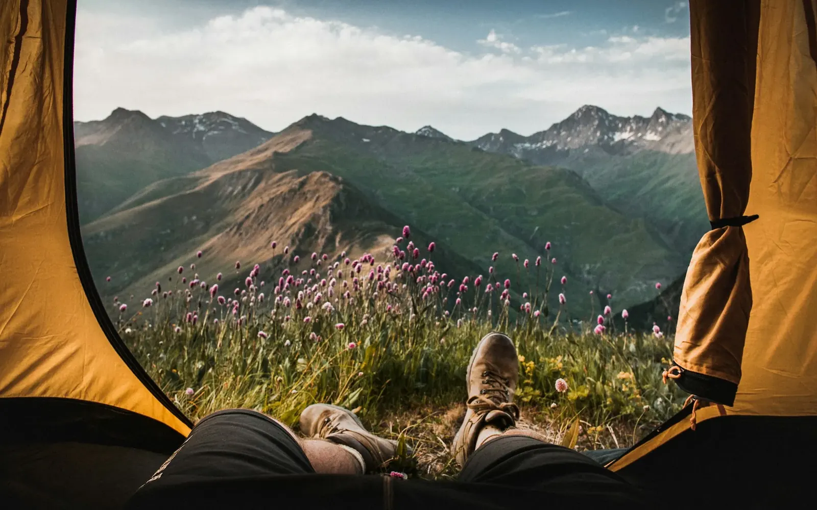 Vista desde una carpa abierta hacia las montañas, con las piernas de una persona acostada
