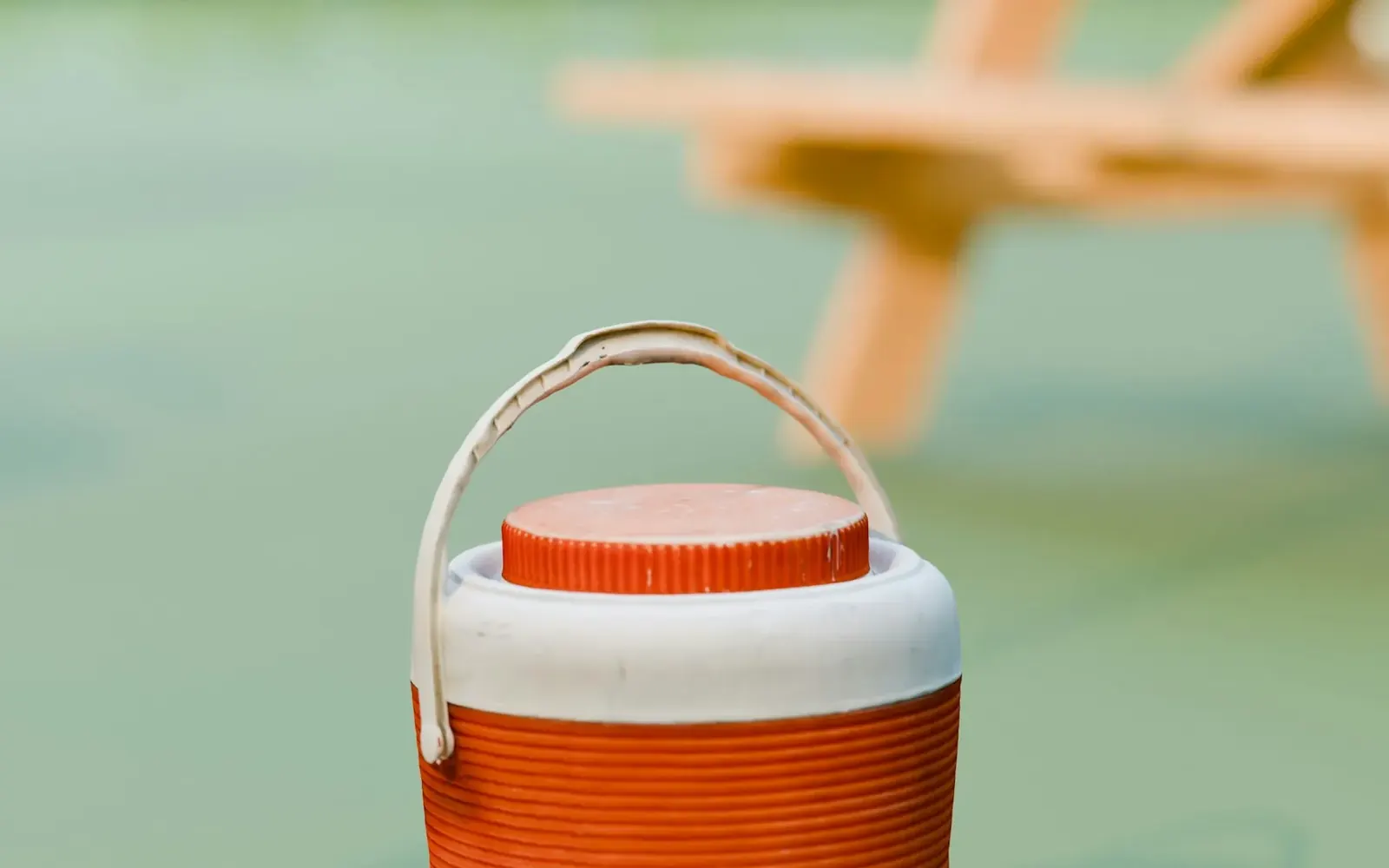 Conservadora portátil naranja y blanca en el pasto, con una mesa de picnic de madera de fondo
