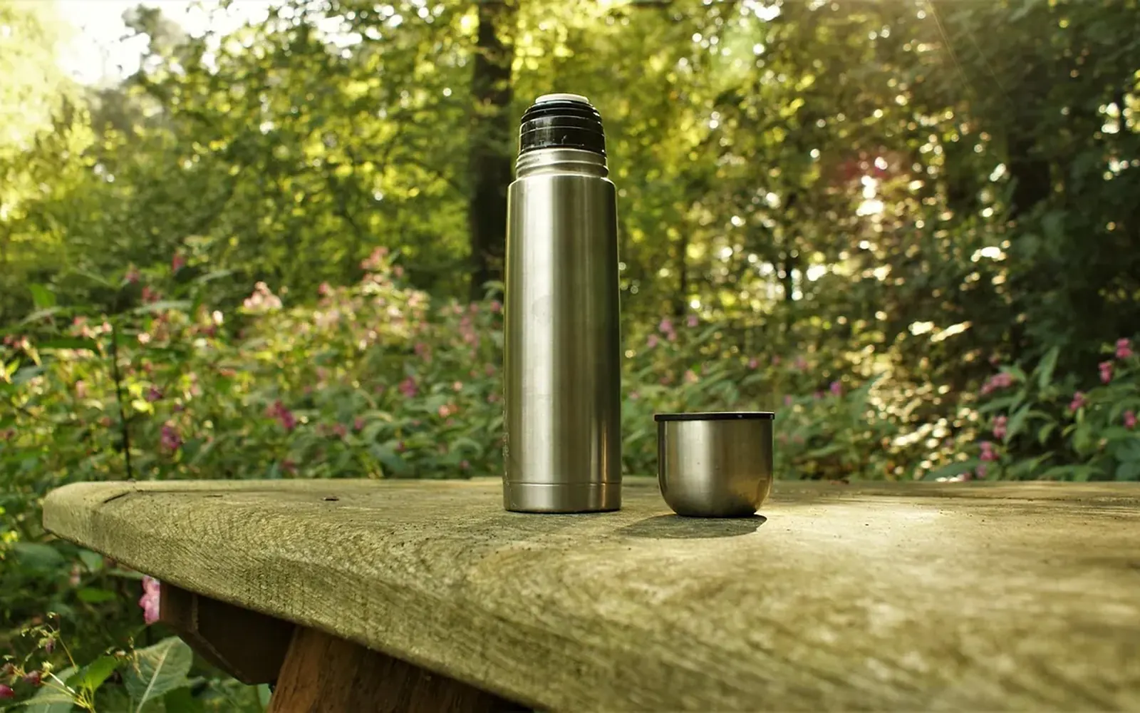 Termo y vaso metálico sobre una mesa de madera en el bosque