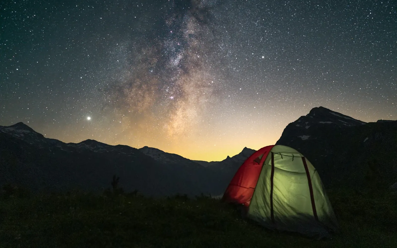 Carpa iluminada bajo la Vía Láctea en la montaña